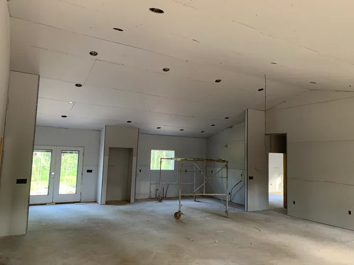 Drywall installed across the home's interior walls and ceiling with a scaffold in the room