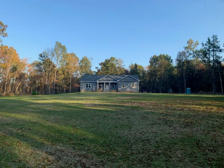 Front view of the house with a grass-covered yard and surrounding trees