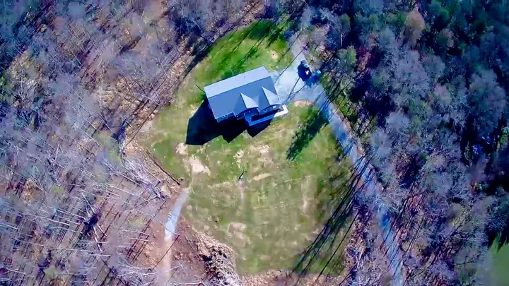 Aerial view of the house, access roadway and clearing within the wooded property